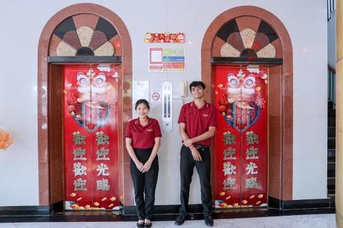 a man and a woman standing between two red doors at Merlin Hotel in Sungai Kolok