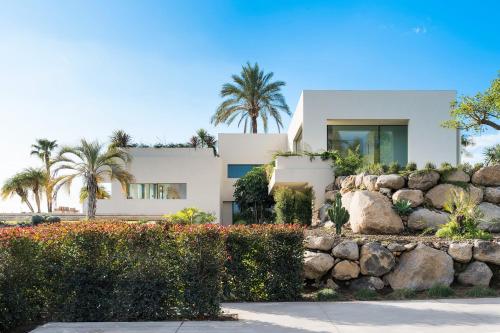 a white house with palm trees and a stone wall at Hermosa in San Leonardello