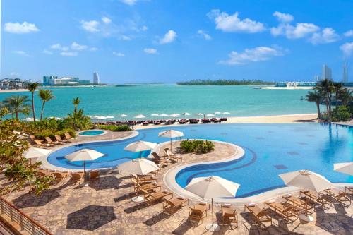 a resort pool with chairs and umbrellas and the ocean at Andaz Family Suites by Hyatt- Palm Jumeirah in Dubai