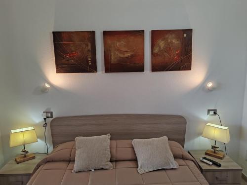 a bedroom with a bed with three paintings on the wall at Villa Orsola in Villaputzu
