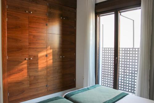 a bedroom with wooden cabinets and a bed and a window at BiBo Suites Real Chancilleria in Granada