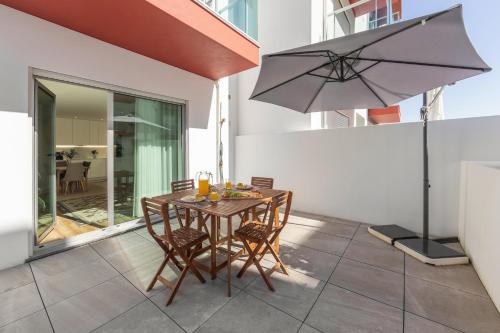 Una mesa con sillas y una sombrilla en un patio. en Consolação Breeze Apartment, en Atouguia da Baleia