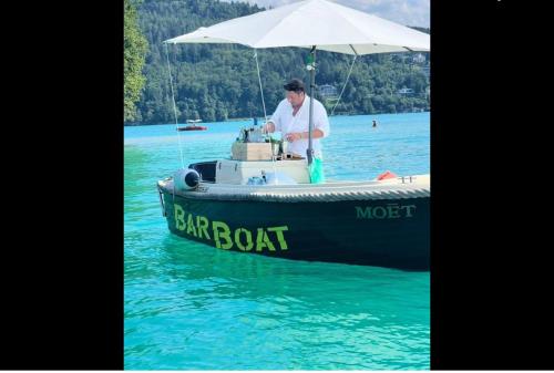 a man in a boat with an umbrella on the water at Strandhaus am Wörthersee in Velden am Wörthersee
