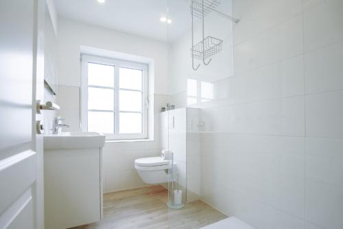 ein weißes Bad mit einem WC und einem Fenster in der Unterkunft Sonnenterrasse - Helle & moderne Ferienwohnung am Meer in Nordstrand