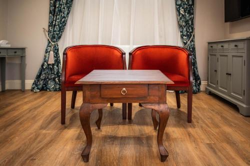 two red chairs and a wooden table in a room at Owston Hall Hotel in Doncaster