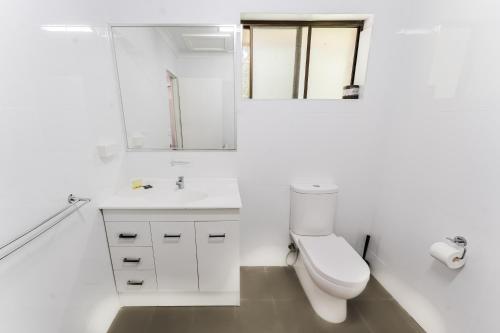 a white bathroom with a toilet and a sink at Country 2 Coast Motor Inn Coffs Harbour in Coffs Harbour