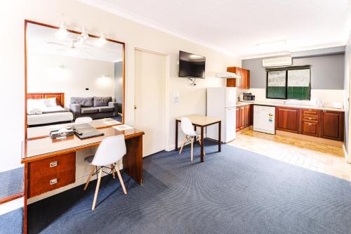 a room with a desk and a bed and a kitchen at Country 2 Coast Motor Inn Coffs Harbour in Coffs Harbour