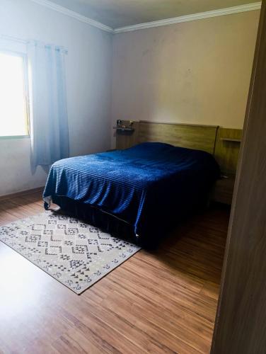 a bedroom with a blue bed and a rug at Quarto Privativo Santa Rita do Sapucaí in Santa Rita do Sapucaí