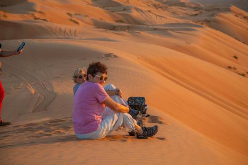 two people sitting on a sand dune in the desert at Sands Dream Tourism Camp in Shāhiq