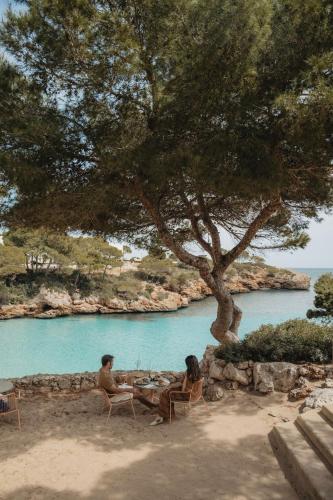 two people sitting at a table under a tree on the beach at Inturotel Cala Esmeralda Beach Hotel & Spa - Adults Only in Cala d´Or