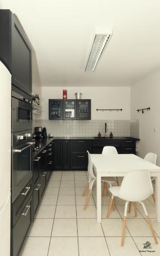 une cuisine avec des armoires noires et une table et des chaises blanches dans l'établissement Maison des viennes, à Saint-André-les-Vergers