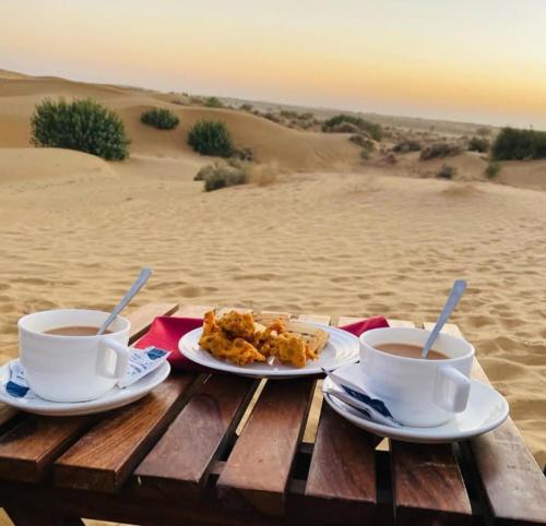 two cups of coffee and food on a table in the desert at Khamma Ghani Resort with pool Luxury camp in Jaisalmer in Jaisalmer