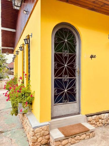 a yellow building with a black door and flowers at Pousada Casinha Amarela - Campos do Jordão in Campos do Jordão