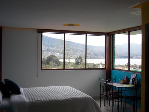 a bedroom with a bed and a table and windows at Green House Araque Inn in Otavalo