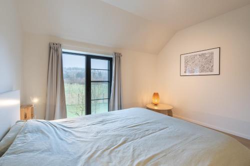 a white bedroom with a large bed and a window at Nature'Hayette in Tenneville