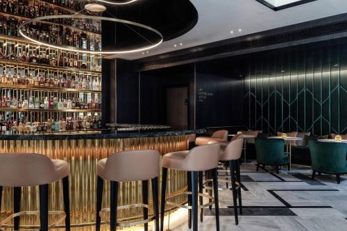 a bar with stools and a wall of liquor bottles at Academias Hotel, Autograph Collection in Athens