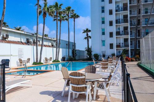 Un patio con mesas y sillas junto a una piscina. en Embassy 402 Condominium Condo, en South Padre Island