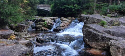 a river with a bridge in the background with waterfalls at U Monoskiera in Hořejší Vrchlabí
