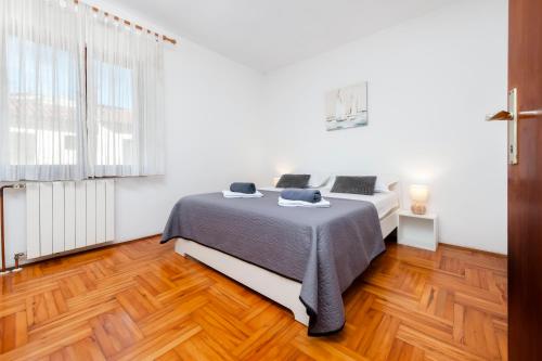 a white bedroom with a bed and a wooden floor at Apartments Luce in Rovinj