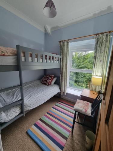 a bedroom with bunk beds and a window and a rug at Cosy Cottage overlooking the Teifi Gorge in Cilgerran