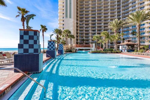 a swimming pool at the resort with palm trees and the ocean at Shores of Panama 727 - Same level parking space! in Panama City Beach