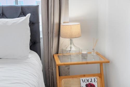 a bed with a table with a lamp on it at Lovely Refurbished 2 Bedroom Apartment in Nottingham