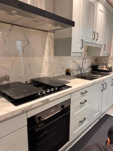 a kitchen with white cabinets and a black stove top oven at Modern House Apartment Stratford E15 London - Sleeps 2 - 9, Fast Links to Central London, Near O2, Greenwich & Olympic Park, Child-Friendly Garden, Free Parking, Free WiFi in London