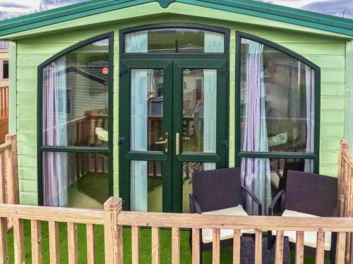 a green shed with a door and two chairs at Skiddaw Lodges- The Lake District in Plumbland