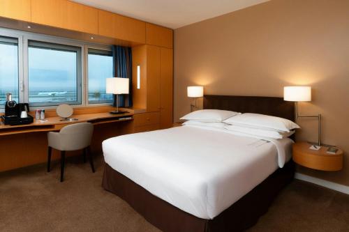 a hotel room with a large bed and a desk and window at Sheraton Paris Charles de Gaulle Airport Hotel in Roissy-en-France