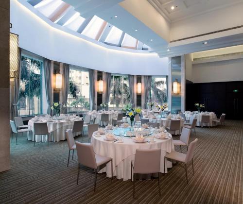 un salón de banquetes con mesas y sillas blancas y ventanas en New World Shunde Hotel, en Shunde
