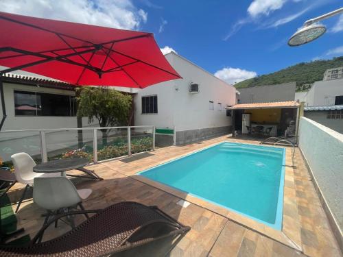 a pool with a red umbrella next to a house at Pousada Paraíso das Águas Capitólio in Capitólio