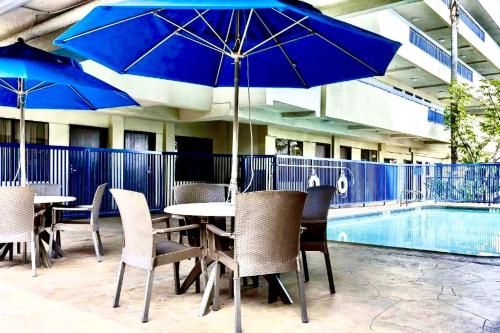 a table and chairs with blue umbrellas next to a pool at Quality Inn & Suites Los Angeles Airport - LAX in Inglewood