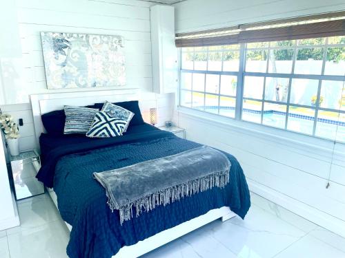 a bedroom with a bed with a blue blanket and windows at Tropical Oasis Private Guest Suite min to Wilton Drive-Ft Lauderdale Beaches in Fort Lauderdale