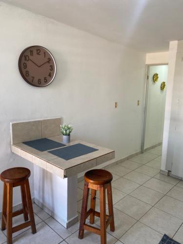 a clock on a wall above a counter with two stools at Suites 115 in Culiacán