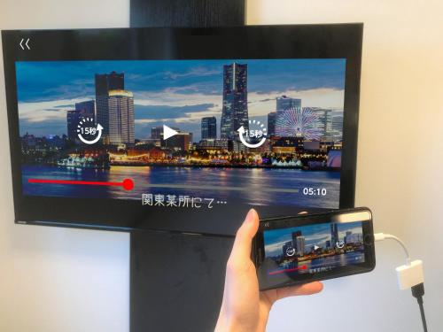 a person holding a cell phone in front of a tv at APA Hotel Omori Ekimae Higashi in Tokyo