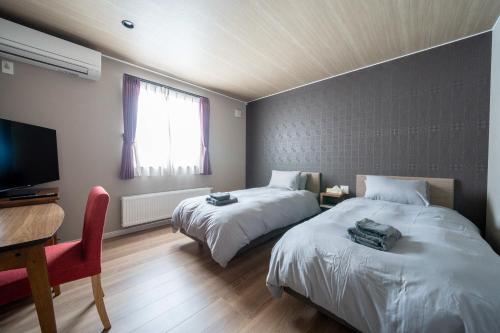 a room with two beds and a desk and a television at THE Sakura in Kami-furano