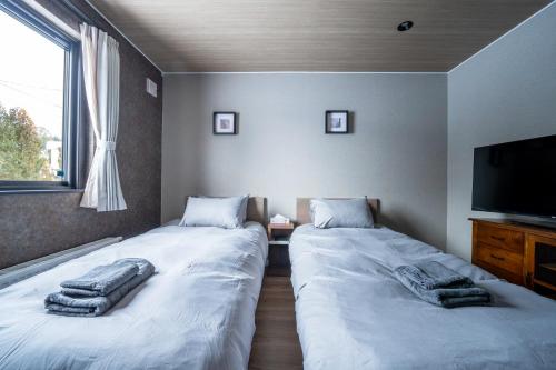 two beds in a room with a flat screen tv at THE Sakura in Kami-furano