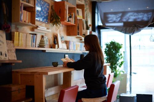a woman sitting at a table reading a book at KARASUYA GuestHouse in Takasaki