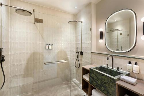 a bathroom with a shower and a sink and a mirror at The College Hotel Amsterdam, Autograph Collection in Amsterdam