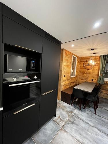 une cuisine avec une armoire noire, une télévision et une table dans l'établissement Le Refuge des Mômes, à Huez