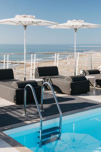 a swimming pool with chairs and umbrellas and the beach at Hotel Marco Polo in Caorle