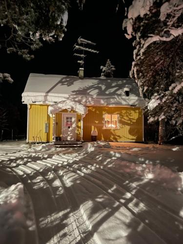 a yellow house with snow on the roof at night at Mysigt hus på hästgård, mellan Jukkasjärvi och Kiruna in Kiruna