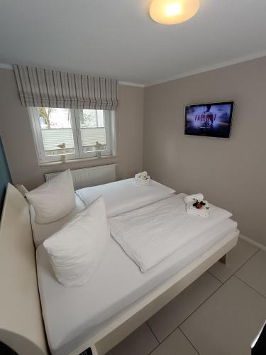 a white bed with white pillows and a tv at Haus Nemo - Appartement 5, Gemütliches Appartement - Strandkorb, strandnah 50 m in Heringsdorf