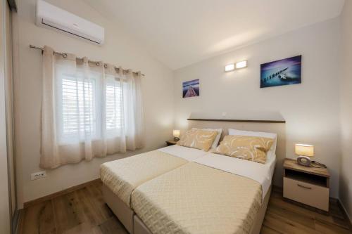 a white bedroom with a bed and a window at Apartmani Savin in Brodarica