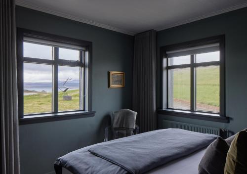 a bedroom with two windows and a bed with a chair at Hvammsvík Nature Resort in Kjósahreppur