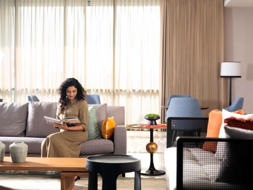 a woman sitting on a couch reading a book at Pullman Chennai Anna Salai - Premium Brand By Accor in Chennai