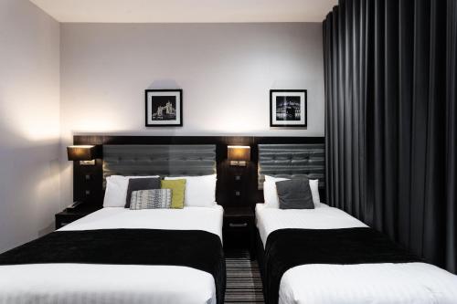 two beds in a hotel room with black curtains at The W14 Kensington in London