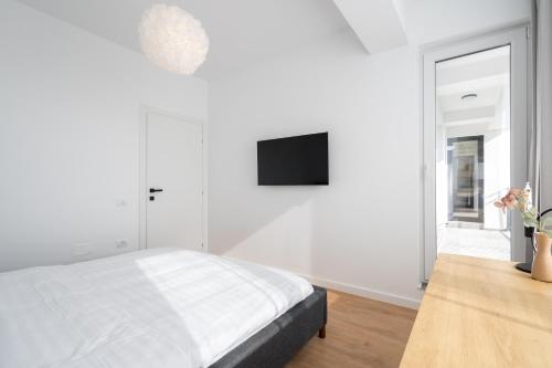 a white bedroom with a bed and a tv on the wall at AeroPrime - LOFT in Tunari
