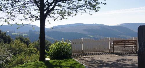 a bench sitting next to a fence with a view of mountains at Waldhaus Ohlenbach in Schmallenberg