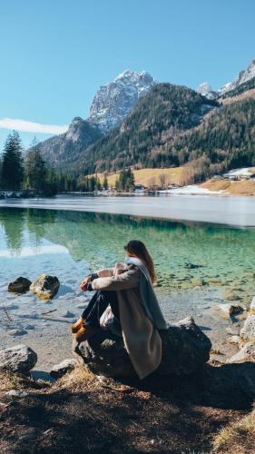 a woman sitting on the shore of a lake at Klosterhof – Alpine Hideaway & Spa in Bad Reichenhall